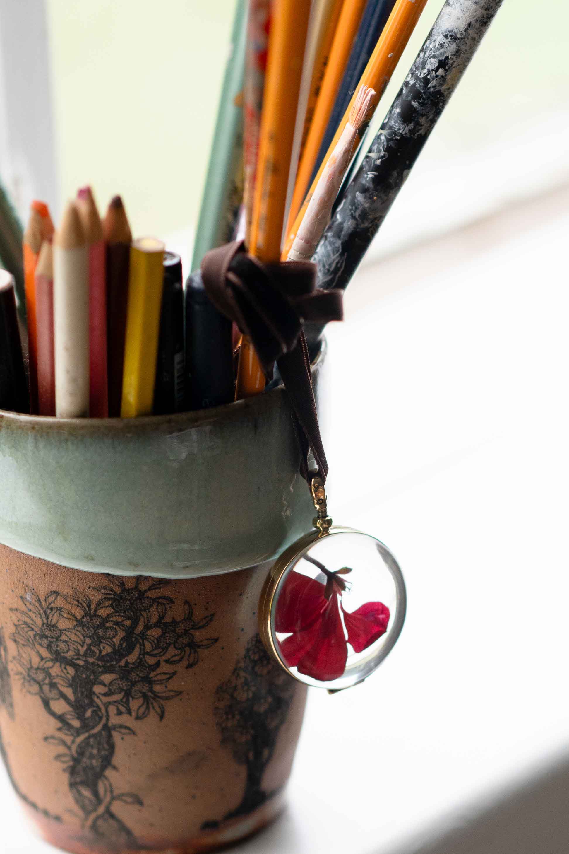 Crystal locket with red flowers and pencils in a pot