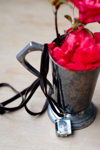 Crystal locket with photo, next to red flowers in a silver cup