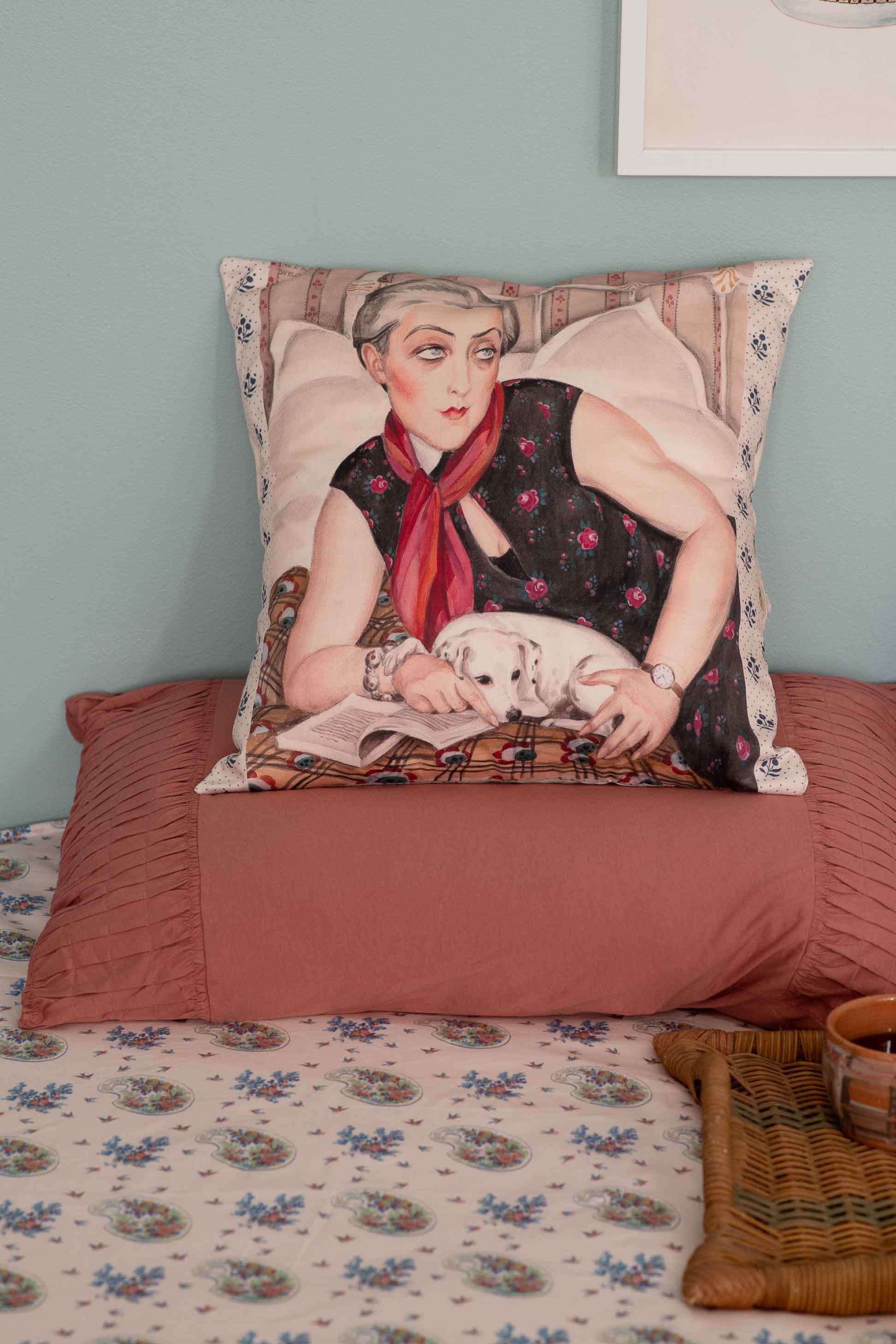Decorative pillow with woman and dog on a bed.
