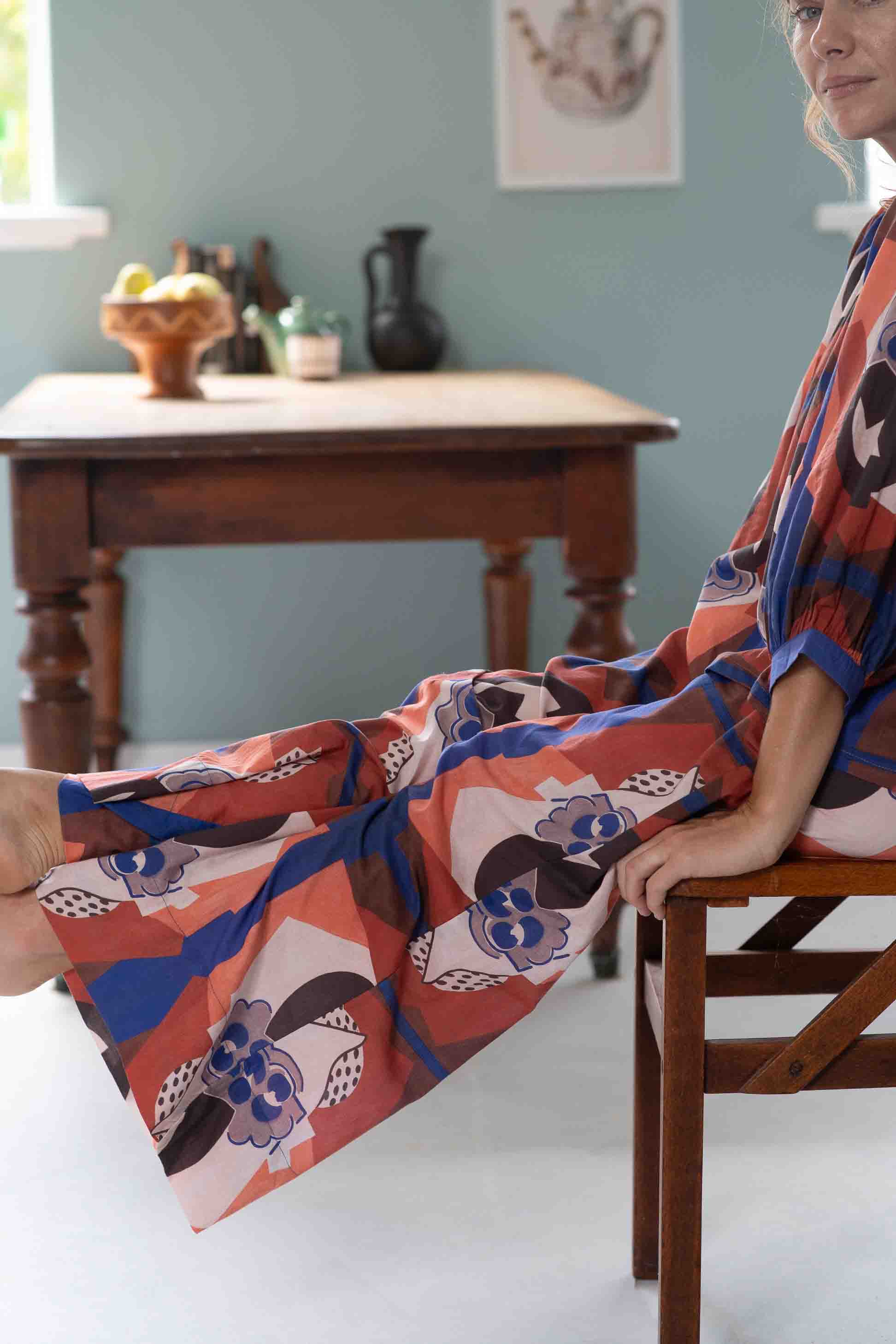 Woman in patterned outfit seated near table.