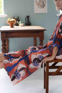 Woman in patterned outfit seated near table.