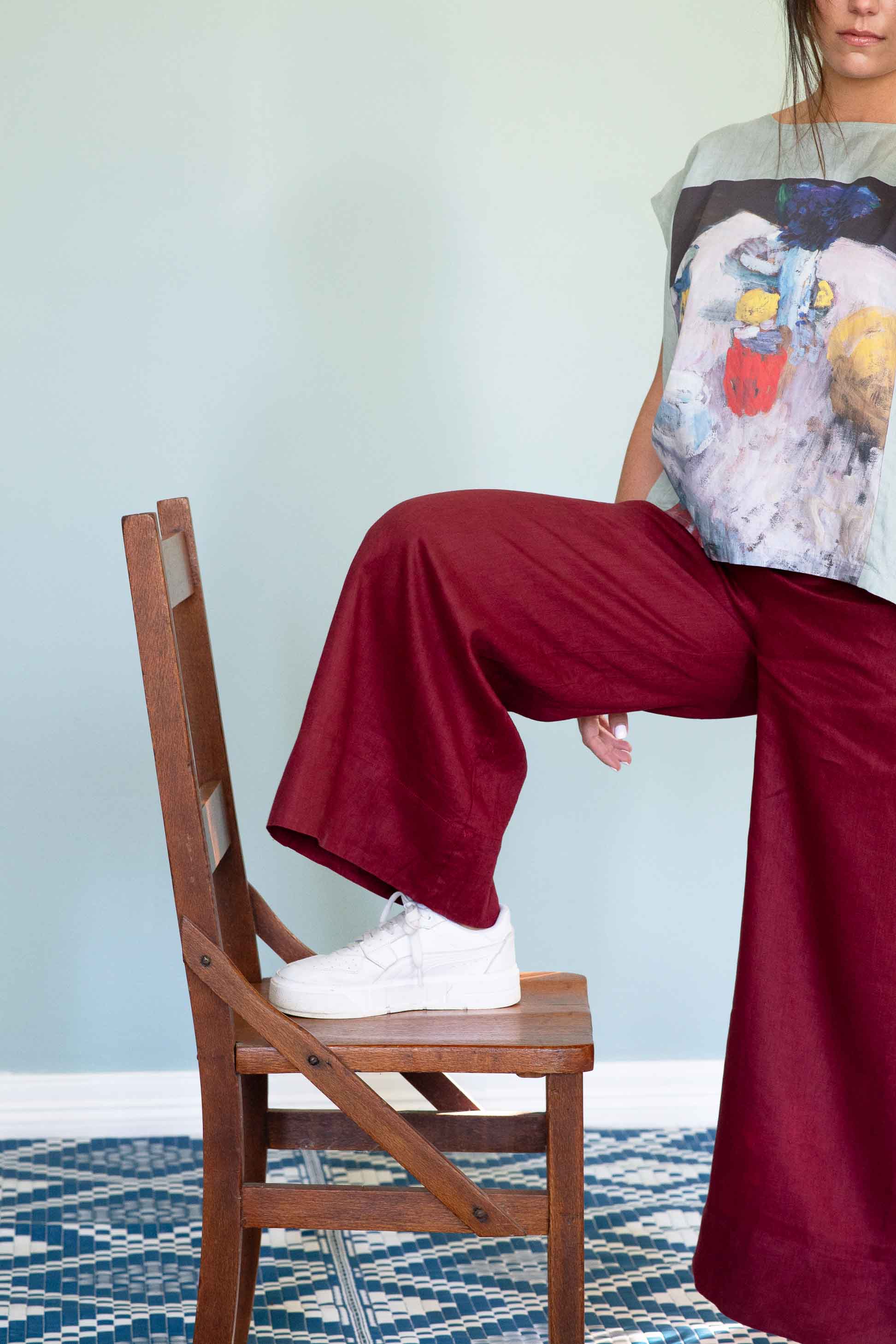 Ollie Red pants with foot on wooden chair.