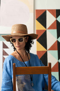 Zahra wearing hat & sunglasses with artwork in background