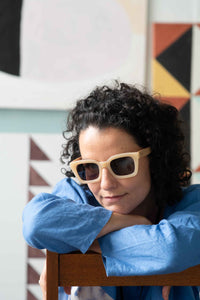 Zahra in sunglasses, leaning on chair, with clouds backdrop