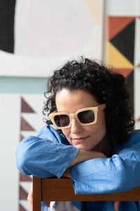 Zahra in sunglasses, leaning on chair, with clouds backdrop