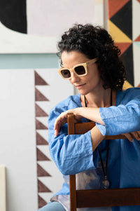 Zahra Fara, wearing sunglasses, leaning on chair in front of clouds-like art.