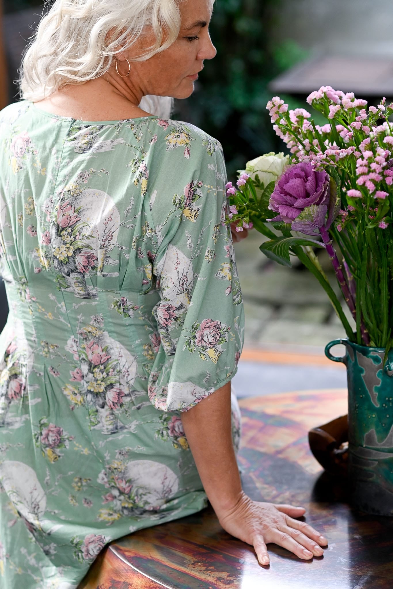 Woman in a floral dress sitting at a table with flowers