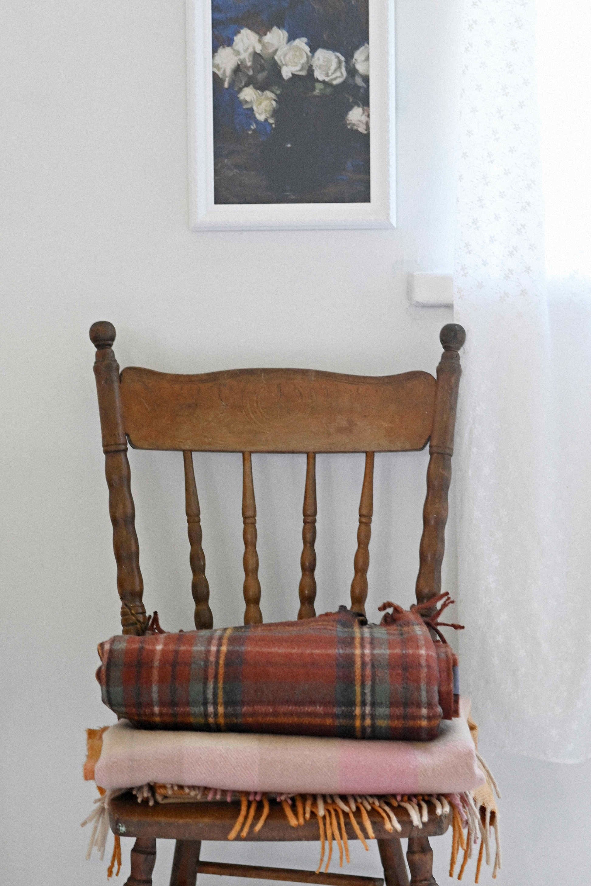 Art print of white roses above a chair with orange gingham blanket.