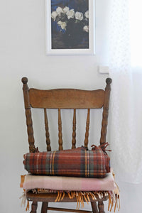 Art print of white roses above a chair with orange gingham blanket.