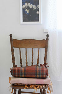 Art print of white roses above a chair with orange gingham blanket.