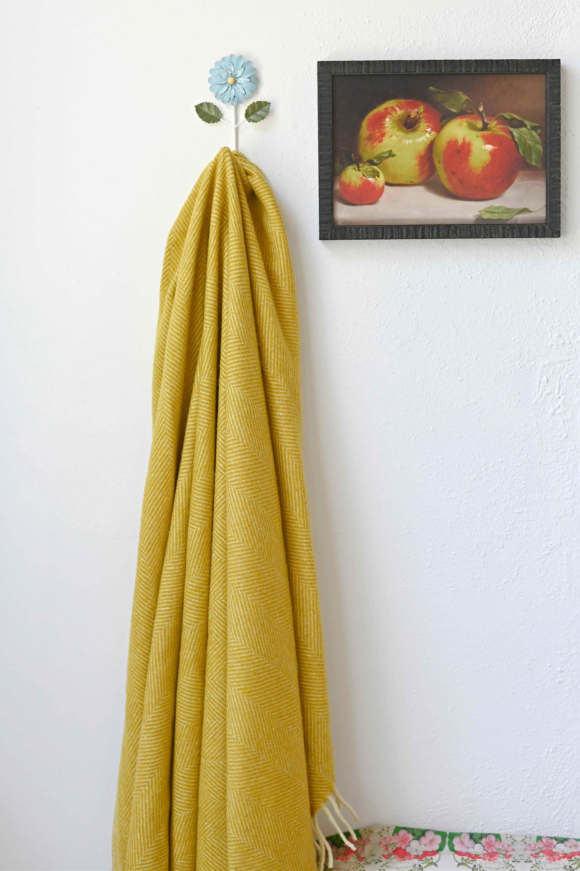 Mustard blanket on wall hook with apple art print.