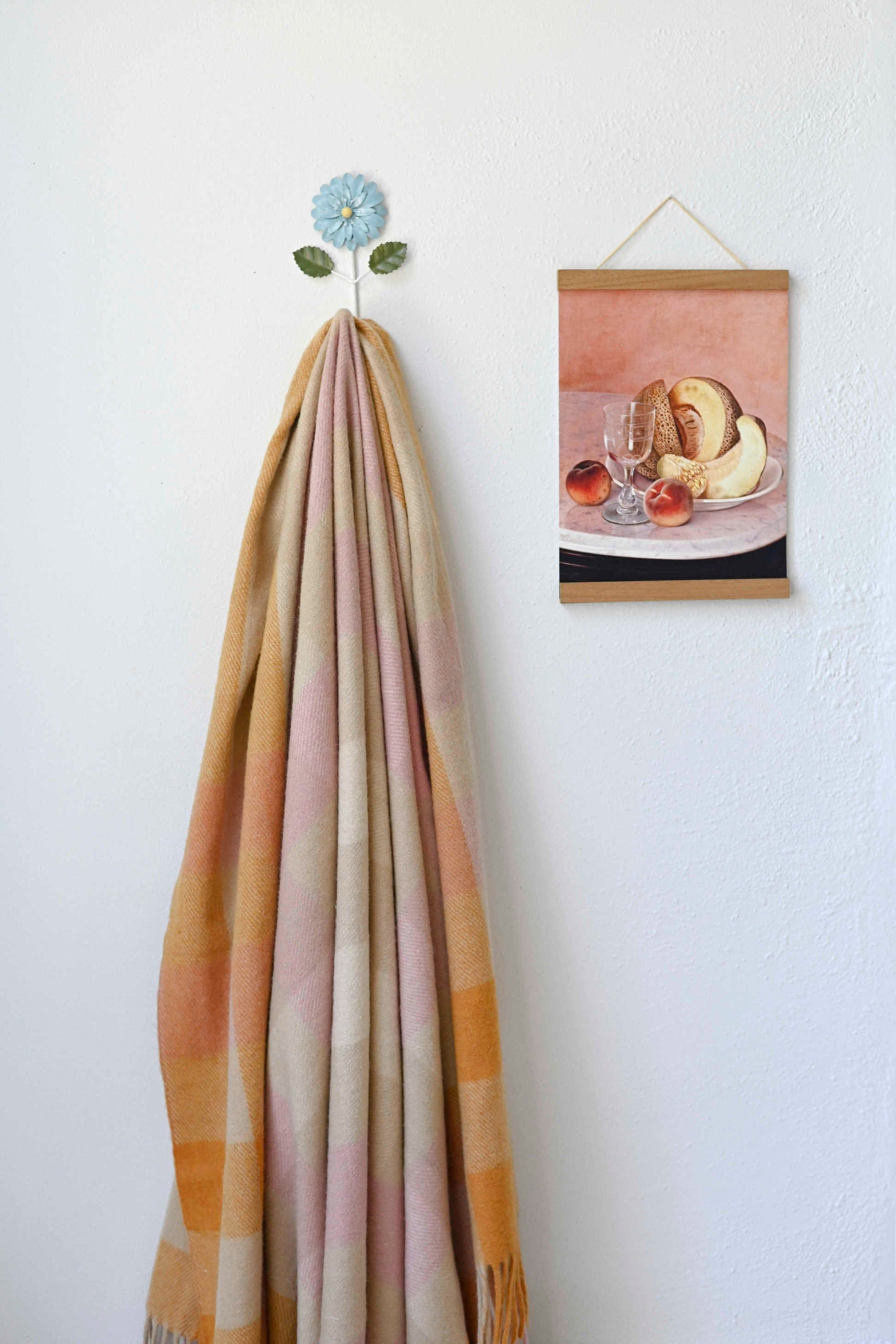 Orange gingham blanket hanging on wall hook with art print.