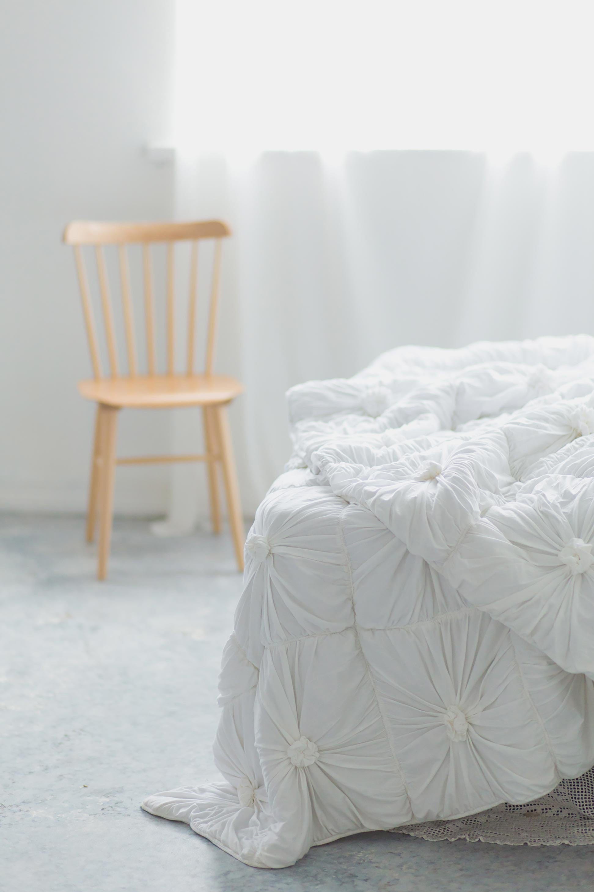 White rosette quilt on bed with wooden chair