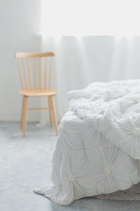 White rosette quilt on bed with wooden chair